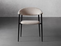 an upholstered chair with black legs and a light colored fabric seat, in front of a gray wall