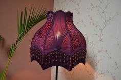 a purple lamp on a table next to a palm tree and wallpapered walls