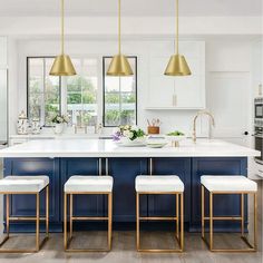 a kitchen with blue cabinets and gold pendant lights hanging from the ceiling over the island