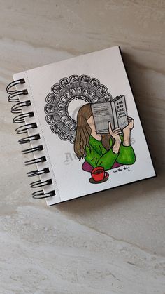 a spiral notebook with a drawing of a woman holding a book on her lap and reading