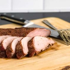 sliced meat sitting on top of a wooden cutting board next to a knife and fork