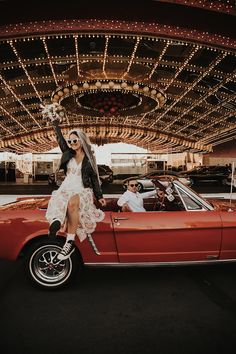 a woman in white dress sitting on top of a red car