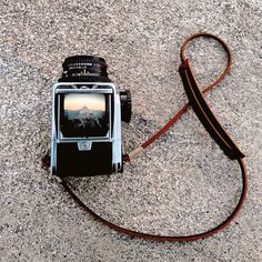 an old camera is laying on the ground next to a brown leather strap that holds it