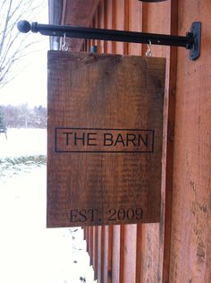 a wooden sign hanging from the side of a building next to a snow covered field