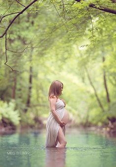 a pregnant woman standing in the middle of a river while holding her belly up to her chest