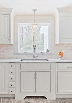 a kitchen with white cabinets and marble counter tops in front of a large window that has a chandelier hanging from the ceiling