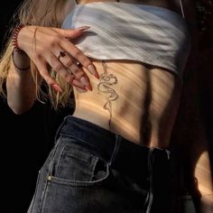 a woman with tattoos on her stomach wearing jeans and a white top is standing in front of a black background