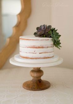 a white cake with succulents on top sitting on a wooden stand in front of a mirror