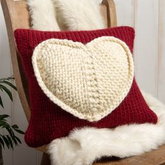 a knitted heart pillow sitting on top of a wooden chair