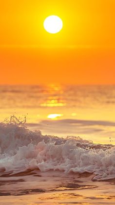 the sun is setting over the ocean with waves crashing in front of it and an orange sky