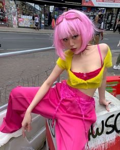 a woman with pink hair is sitting on a wall in the street and posing for a photo