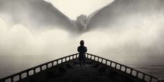 a person standing on a bridge looking at a large dragon in the foggy sky