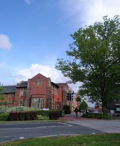 an old red brick building sitting on the side of a road next to a lush green tree