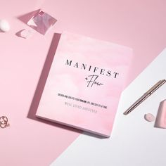 a pink book sitting on top of a white table next to some makeup and other items