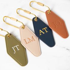 three different colored luggage tags with the letters at and t in gold, white, blue, and pink