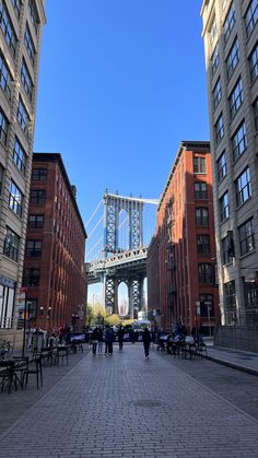 people are walking down the street in front of some tall buildings and a suspension bridge