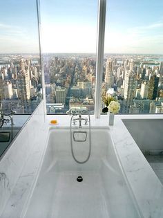 a bathtub in front of a large window overlooking a cityscape and skyscrapers