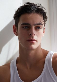 a young man in a white tank top looking at the camera