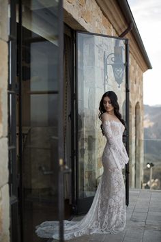 a woman in a white wedding dress standing by a glass door and looking at the camera