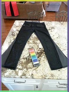 a pair of black jeans sitting on top of a counter next to a rainbow colored remote control