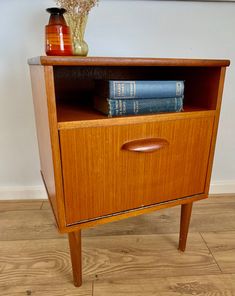 a wooden cabinet with two books on top and a vase filled with flowers next to it