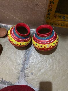 two red and yellow vases sitting on the ground next to some brown bowls with lids