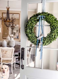 a dog sitting in front of a door with a wreath hanging on it's side