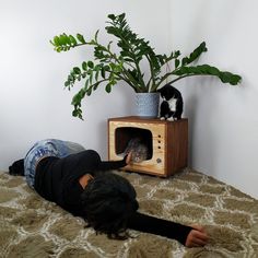 a woman laying on the floor next to a cat in a small wooden litter box