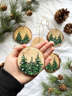 someone is holding some ornaments in their hand and pine cones are on the table next to them