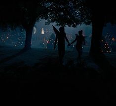 two people holding hands in the dark with trees and lights behind them at night time