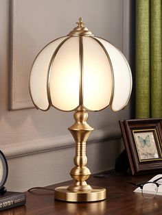 a table lamp sitting on top of a wooden desk next to a framed photograph and clock