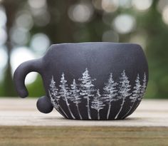 a black cup with trees painted on it is sitting on a wooden table in front of the camera