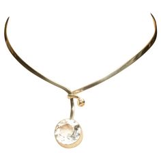 This neck ring is a sleek, silver neck ring that encircles the wearer's neck with a clean and modern design. It has a rigid, collar-like shape that opens at the front, allowing it to wrap comfortably around the neck. A single, large, round rock crystal is set at the front, adding a striking focal point to the piece. When worn, the neck ring sits gracefully at the base of the neck, with the gemstone resting just below the collarbone, providing an elegant and sophisticated look. Pair this neck ring with a chic cocktail dress for an art gallery opening, or let it be a statement piece with a crisp white blouse for a fresh take on office elegance. Gert Thysell was a Swedish master silversmith who worked in Malmo, Sweden and was one of the leading Swedish jewelry-makers during the 1970s. Art Gallery Opening, Swedish Jewelry, Malmo Sweden, Cocktail Chic, Gallery Opening, Chic Cocktail Dress, Crisp White Blouse, Neck Ring, Round Rock