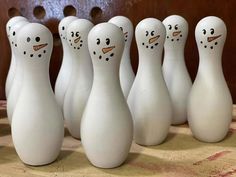 several white bowling pins lined up in a row with faces drawn on them and snowmen painted on the sides