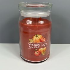 a candle that is sitting on a table with some apples in the jar next to it