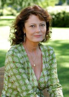 a woman sitting on top of a brown chair in a green shirt and white pants