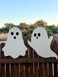 two white ghost cutouts sitting on top of a wooden fence