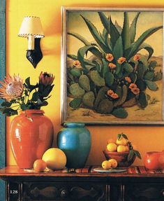 an arrangement of vases and fruit sit on a table in front of a painting