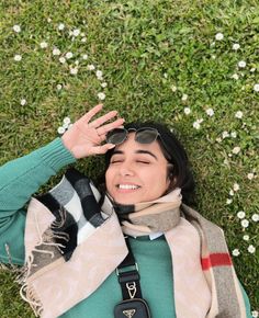 a woman laying in the grass with her hands up to her face and wearing sunglasses