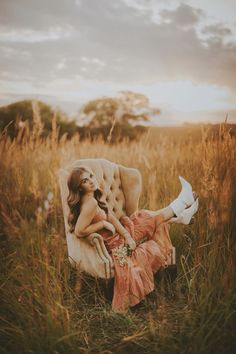 a woman is sitting on a chair in the middle of a field with tall grass