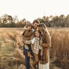 a man and woman holding two small children while standing in a field with tall grass