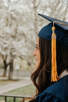 a woman wearing a graduation cap and gown looking off into the distance with trees in the background