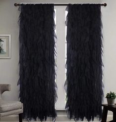 black ruffled curtains hanging in front of a white wall with a chair next to it