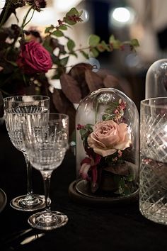 an arrangement of wine glasses and vases on a table with flowers in the glass dome