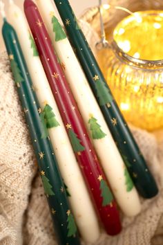 three candles with christmas decorations on them sitting next to a glass vase and candle holder