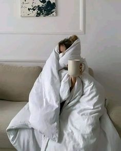 a person wrapped in a blanket and holding a coffee cup under their arm while sitting on a couch