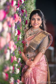 a woman in a pink and gold sari posing for the camera with flowers behind her