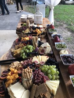 a wooden table topped with lots of different types of cheeses and fruit on top of it