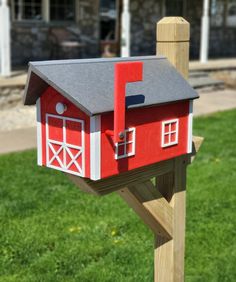 a red and white mailbox sitting on top of a wooden post in front of a house