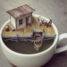 there is a miniature house on top of a coffee cup with people in the boat